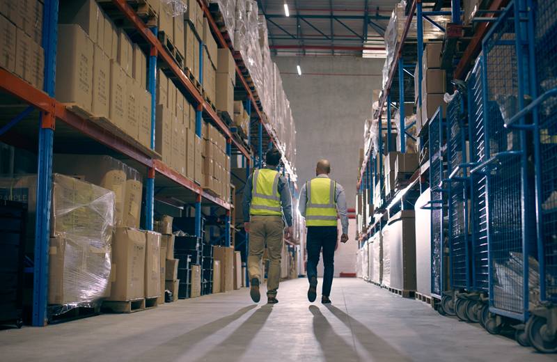Long warehouse aisle with high pallet racking and two staff members